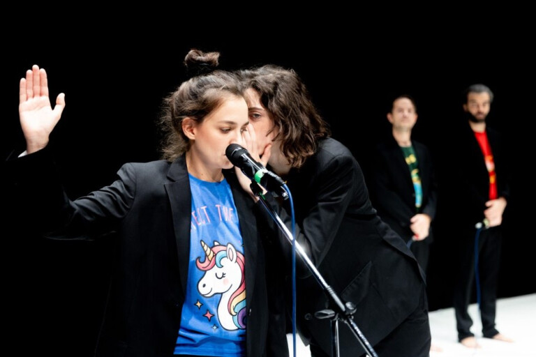 Momento del laboratorio teatrale Parole da rubare di Caterina Marino. Una ragazza bisbiglia all'orecchio di un'altra che è posizionata davanti a un microfono