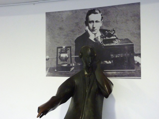 Foto giovanile di Guglielmo Marconi all'epoca dei primi esperimenti con le onde radio e statua commemorativa 