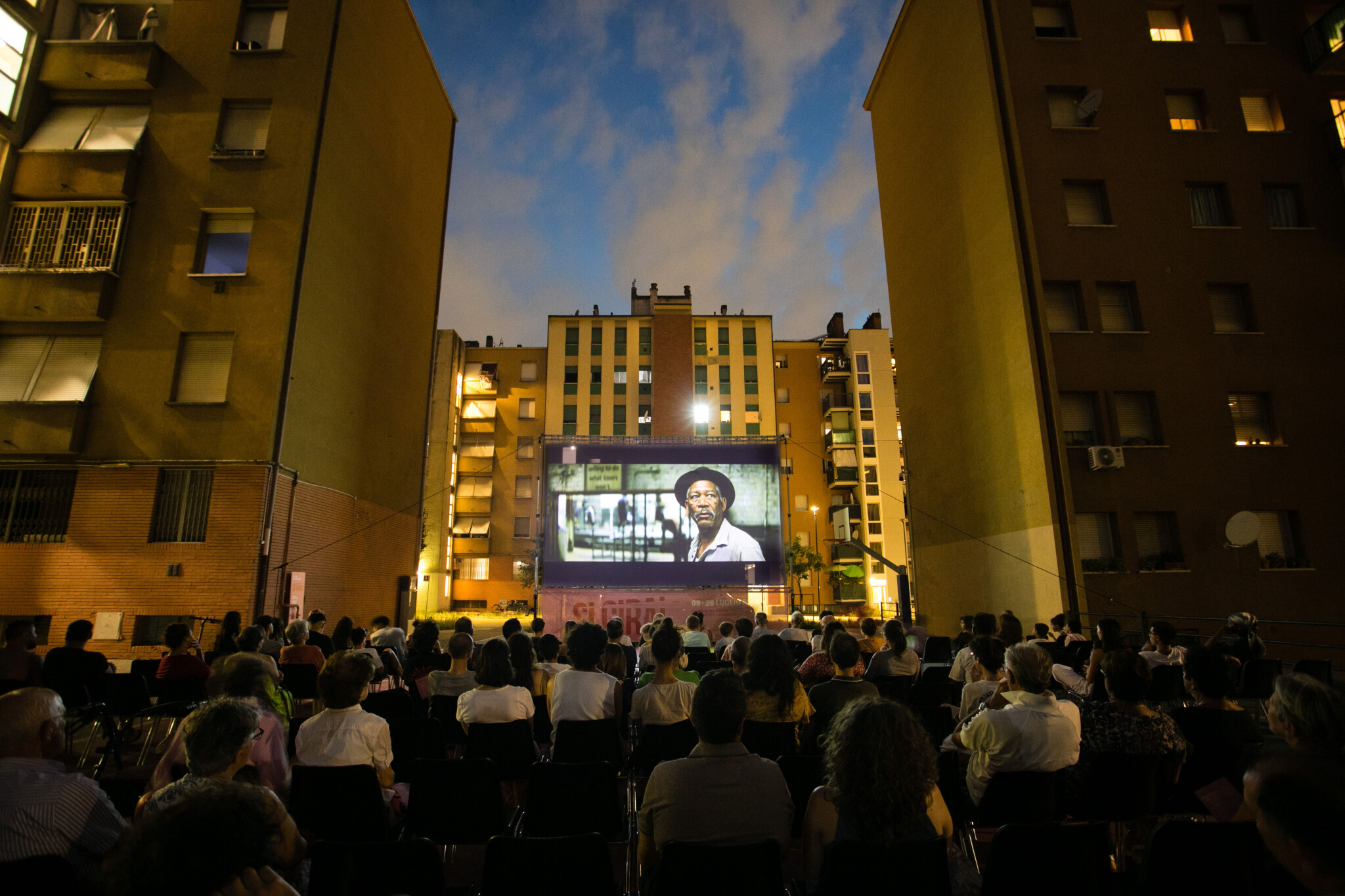 Proiezione della rassegna cinema all'aperto Si Gira! in un cortile tra i palazzi delle Popolarissime a Bologna