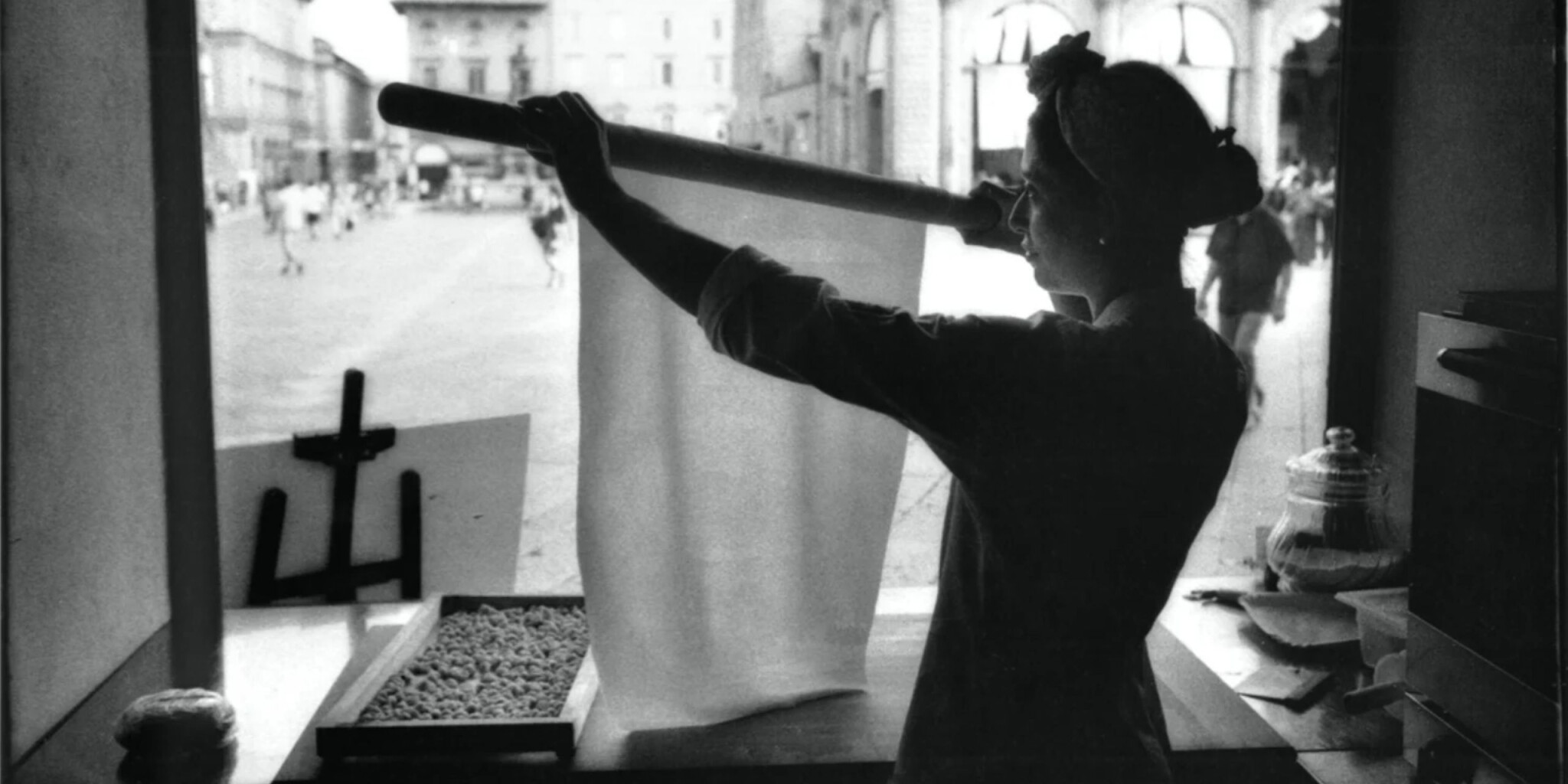 Sfoglina solleva una sottile sfoglia di pasta fresca con il matterello davanti alla vetrina del laboratorio